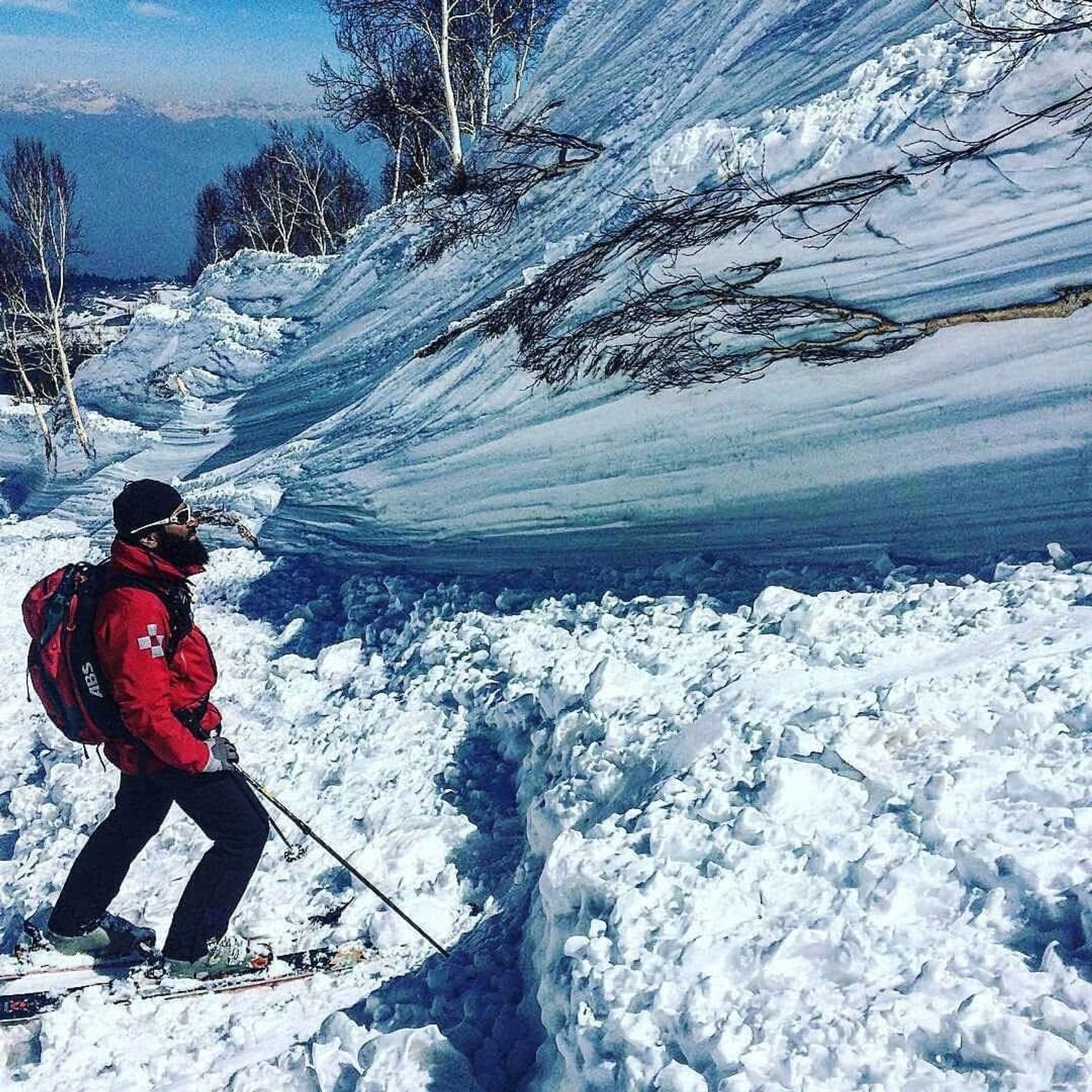 A skier standing beside a large avalanche debris field, with broken blocks of snow and an exposed fracture line.