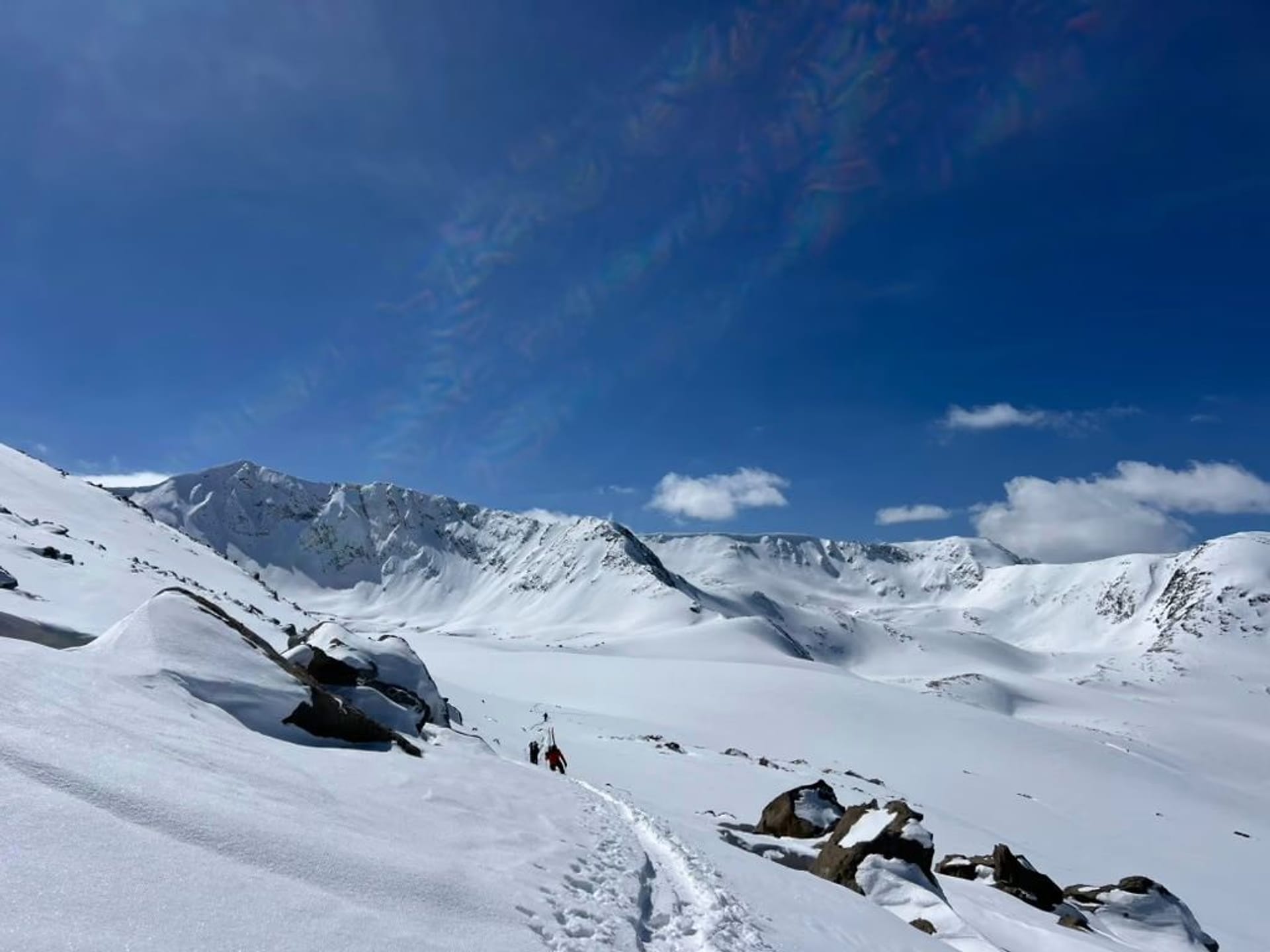 A wide open snow basin scattered with rock outcrops, with ridgelines running to the horizon under a clear sky.
