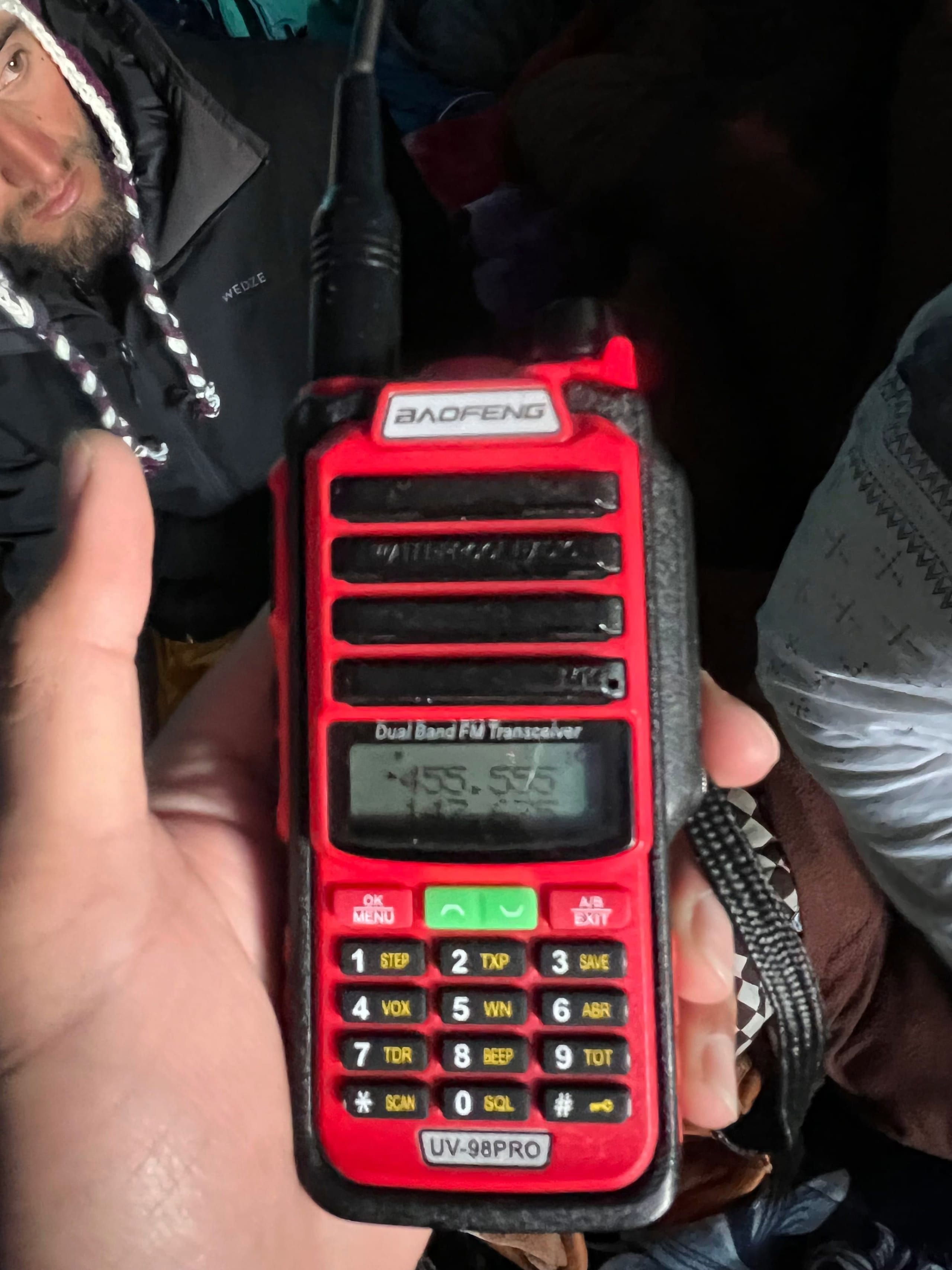 A gloved hand holding a handheld two way radio tuned to a frequency, used for group communication on the mountain.