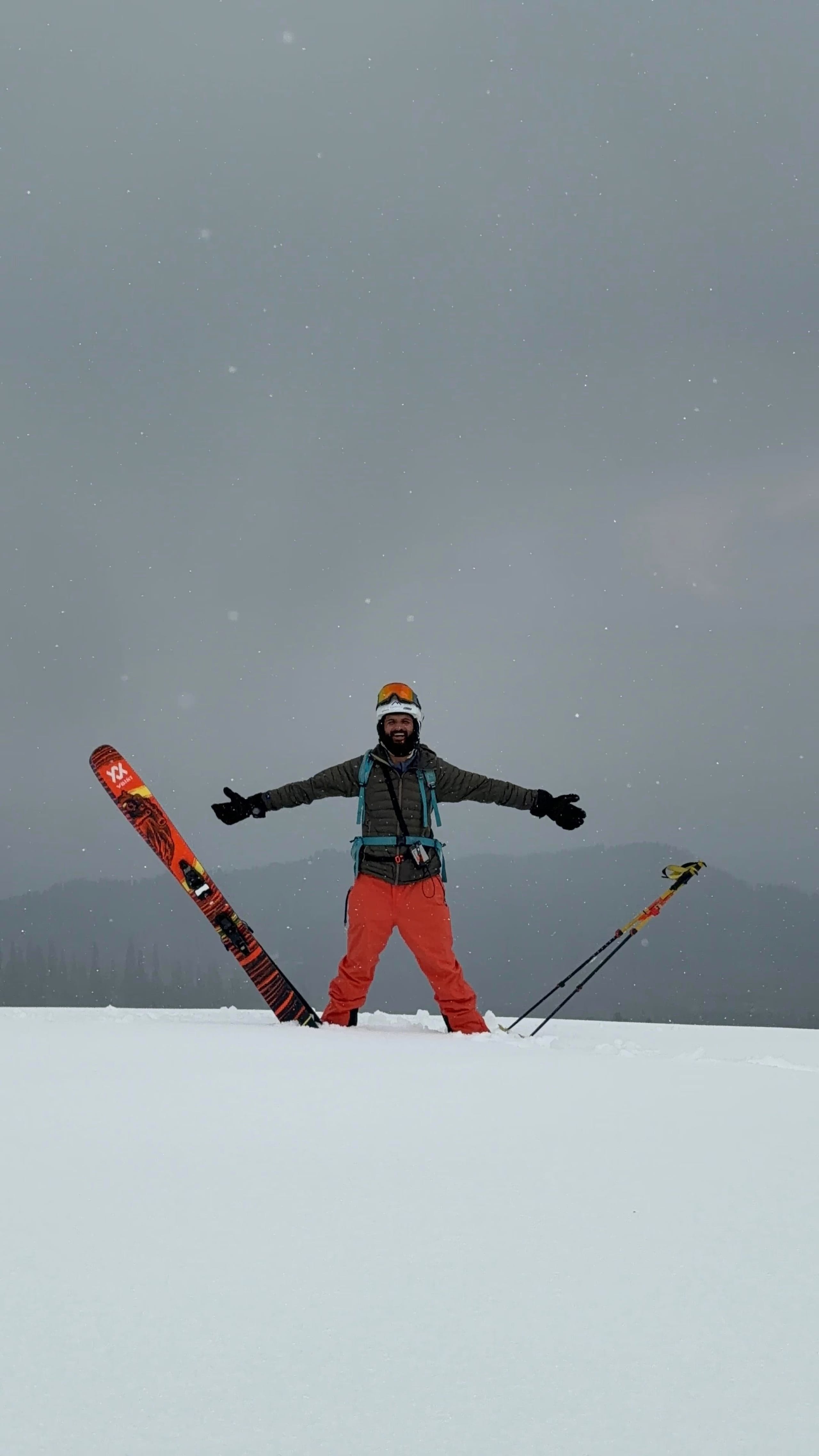 A skier standing with arms outstretched and skis planted either side of them in flat light.