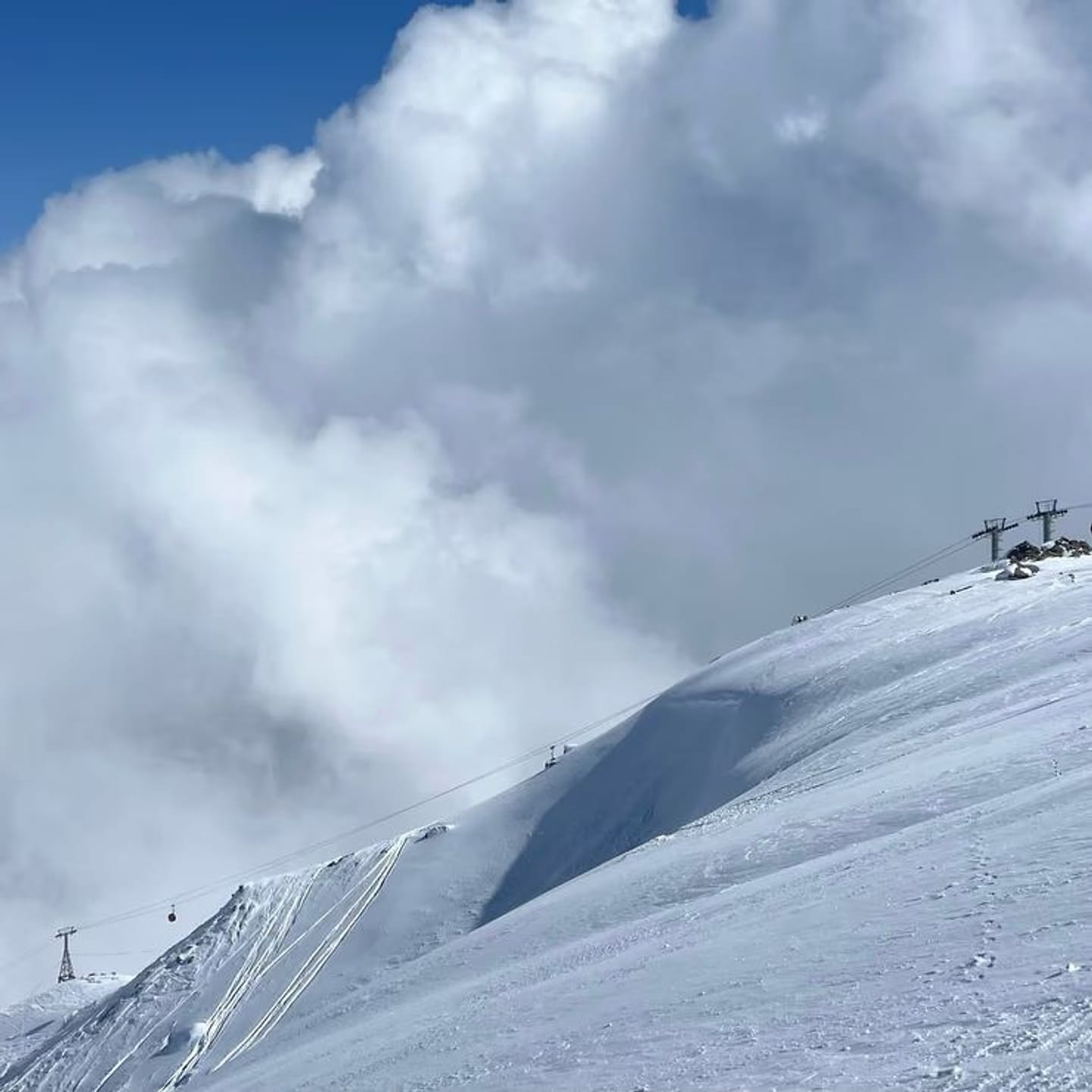A snow ridge on Mt Apharwat with a lift pylon and cloud spilling over the crest on a sunny day.